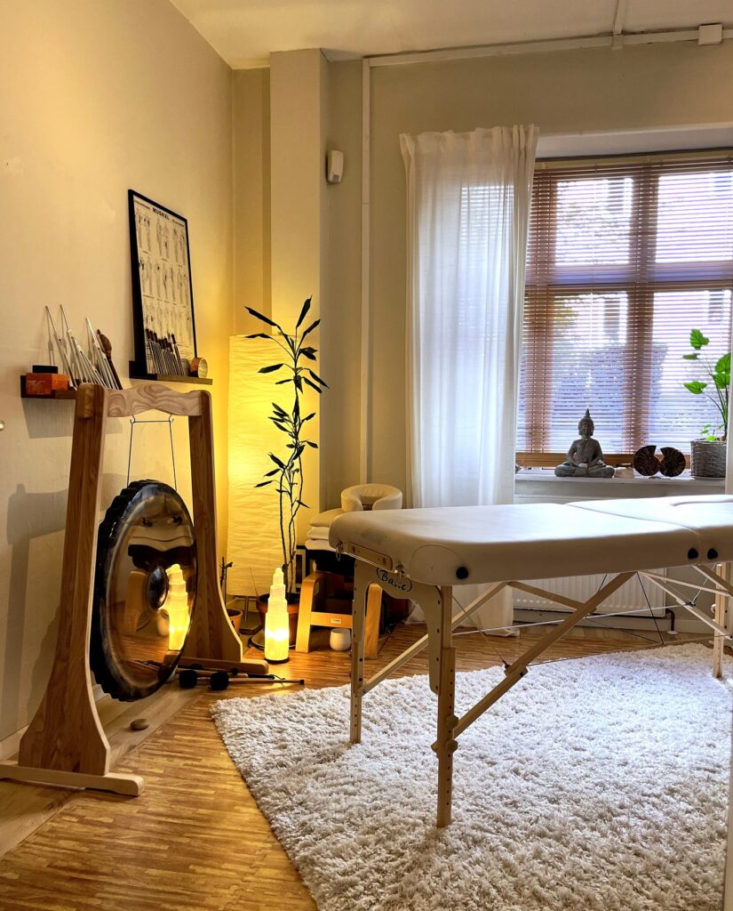 HPH_TreatmentRoom_vertical_retouched - Your Unfolding Self Massage Therapy Room with a Padded Table White Rug Warm Lighting and Plants by a Window with Blinds and a Buddha Statue Nearby Your Unfolding Self